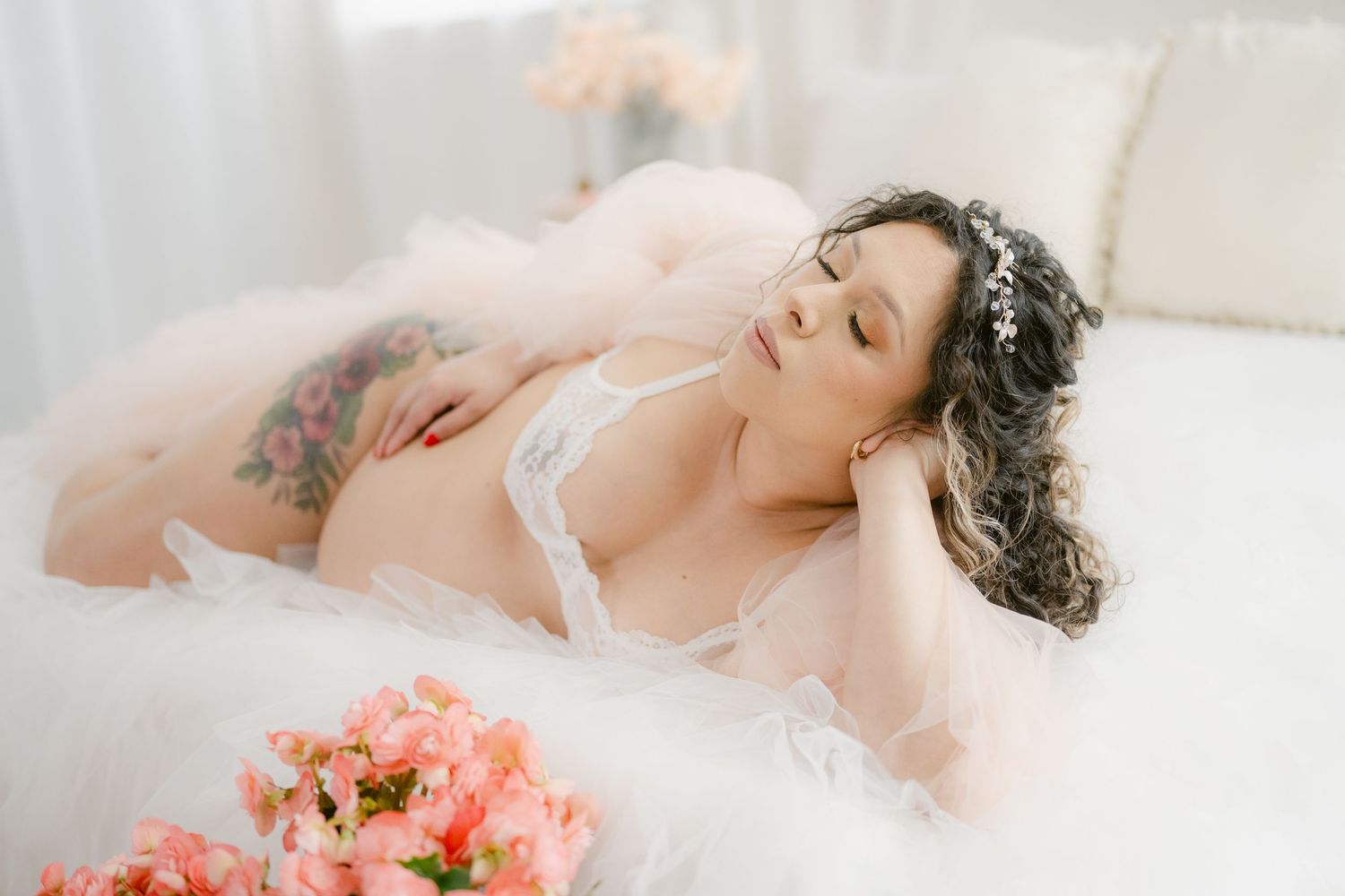 Ethereal boudoir photo featuring soft tulle and delicate pink flowers against light backdrop.