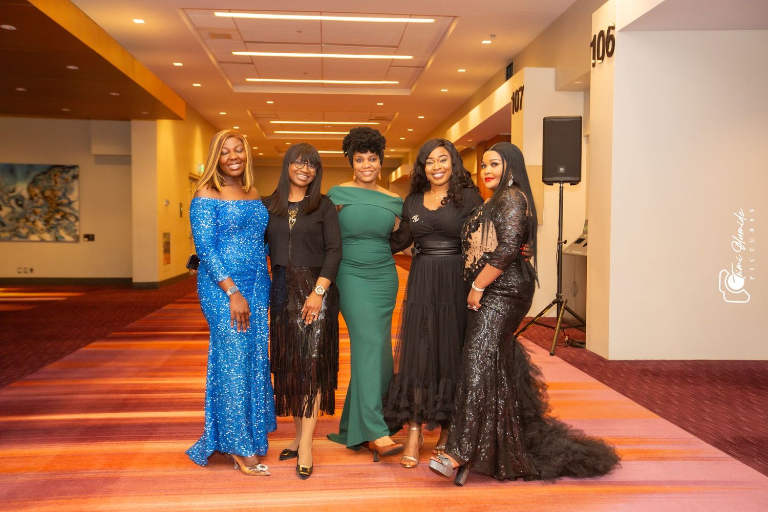 A group in formal evening attire poses together at an elegant event with warm lighting and wooden floors.