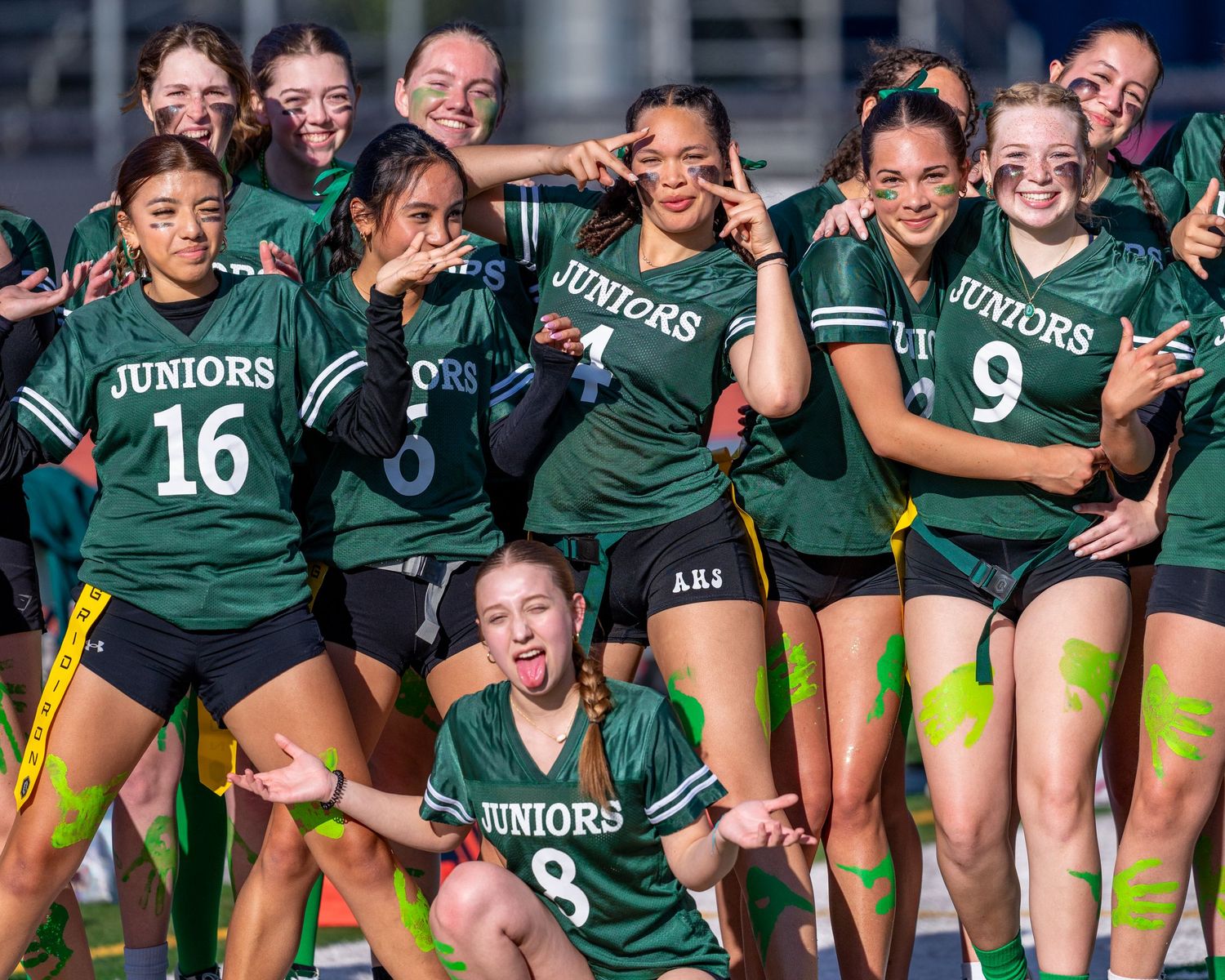 Green uniformed Junior soccer team posing together for fun group photo on field.