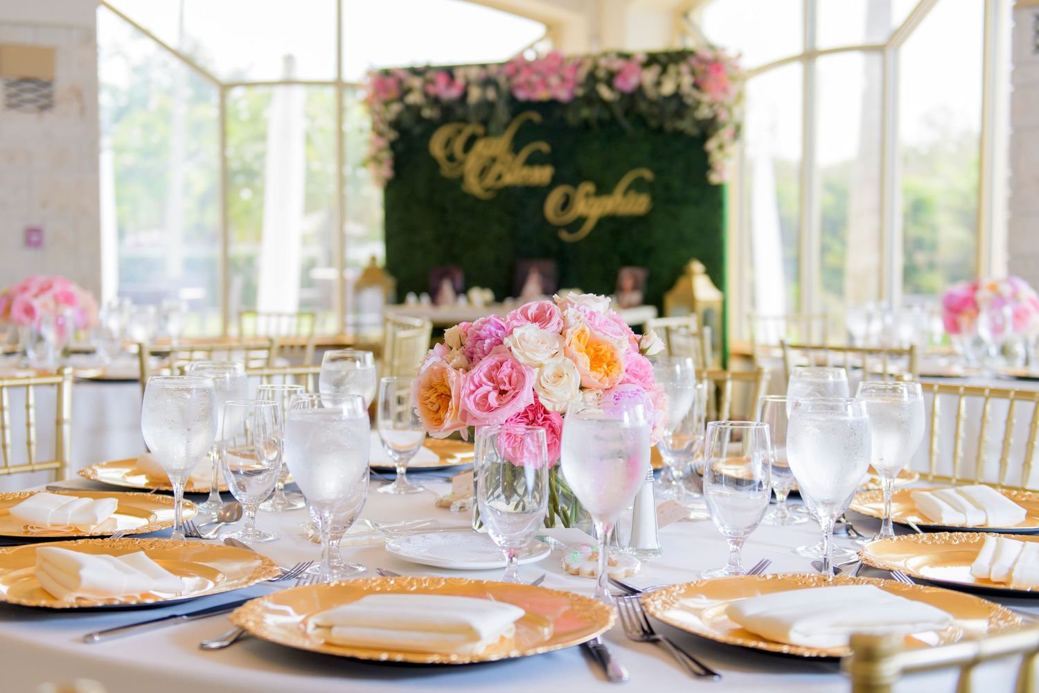 Elegant wedding reception table setting with pink floral centerpiece, gold charger plates and crystal glassware.