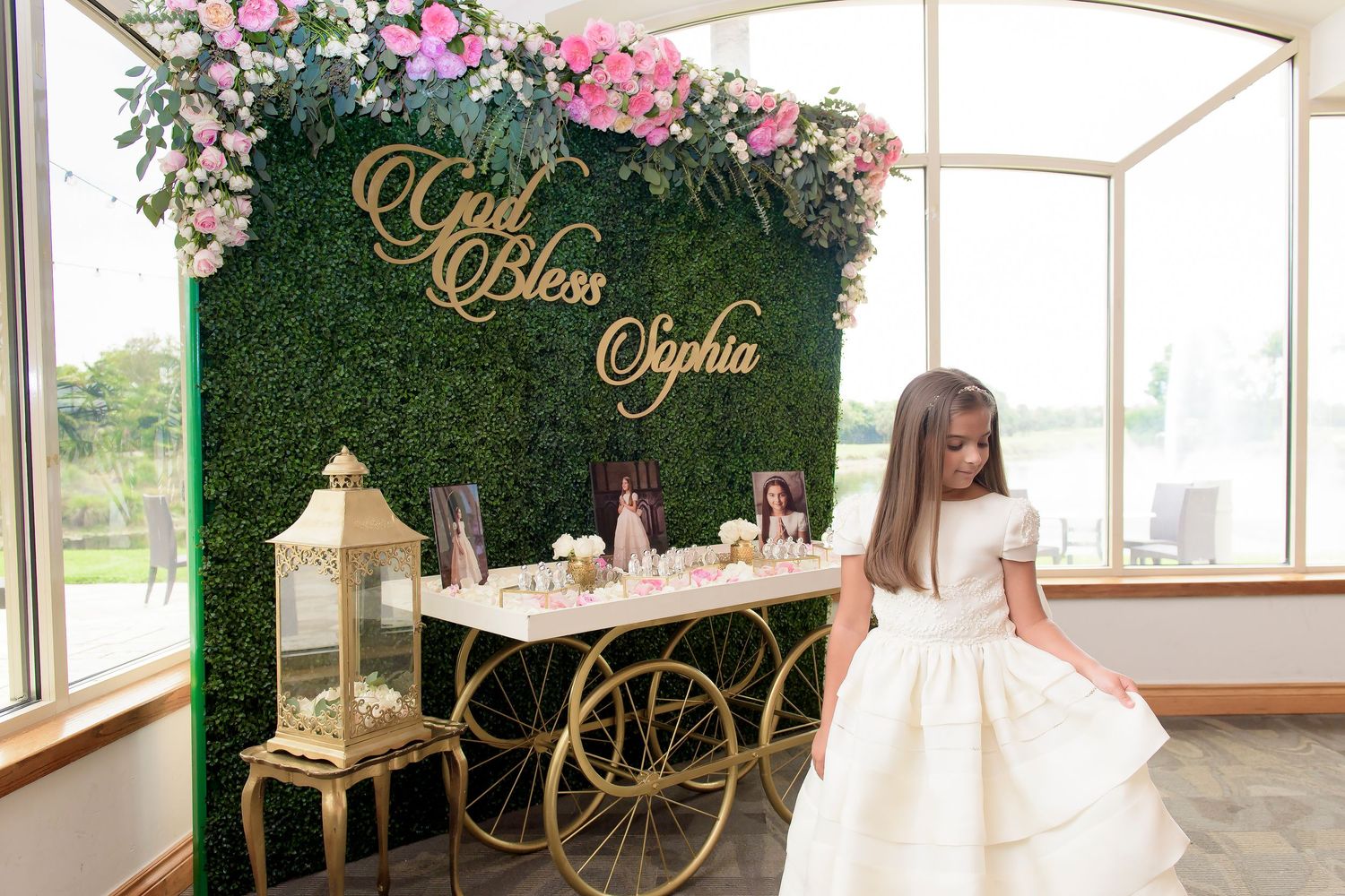 Green hedge wall with gold lettering and decorative cart display for special event.