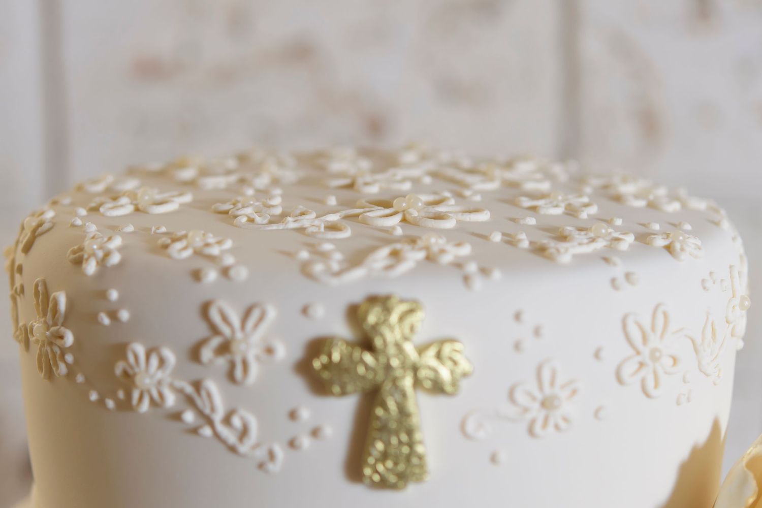 White fondant cake decorated with delicate flower patterns and a gold cross.