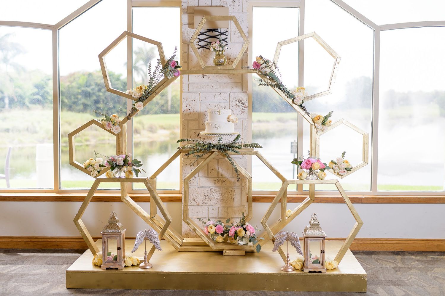 Modern geometric gold display backdrop with hexagonal shelving and floral accents.