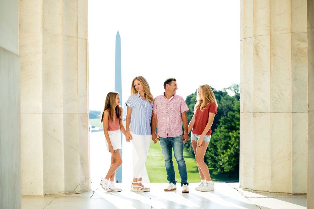 A family between columns at the Lincoln Memorial with the Washington Monument visible in the background, by Justin Baker Photography.