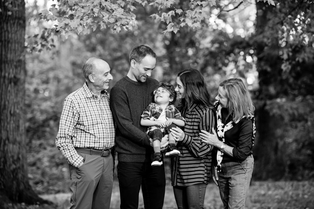 Family gathered together in a park, smiling and interacting with young child in a sweet moment, captured by Justin Baker Photography.