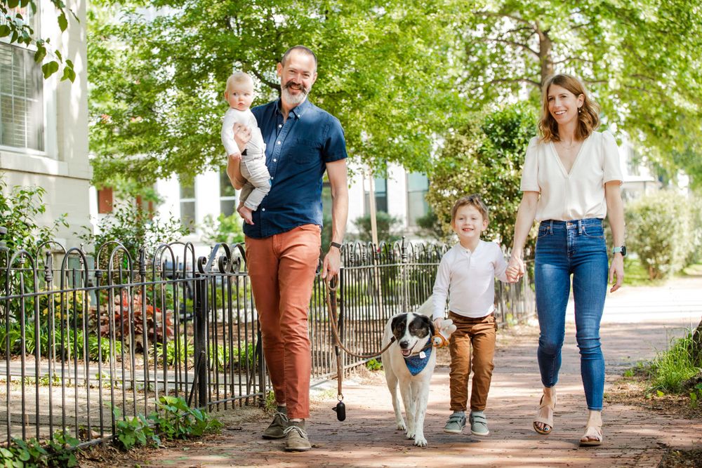 A family takes their dog for a walk along a tree-lined residential sidewalk on a sunny day in DC, by Justin Baker Photography.