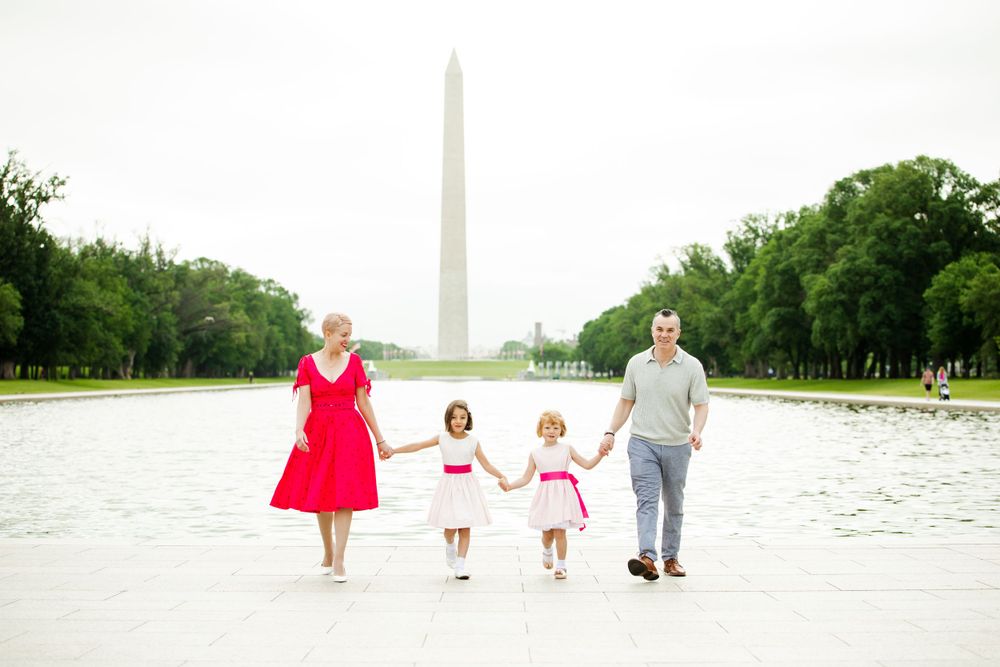 Family holding hands while walking by Reflecting Pool with Washington Monument in background, wearing coordinated outfits, by Justin Baker.