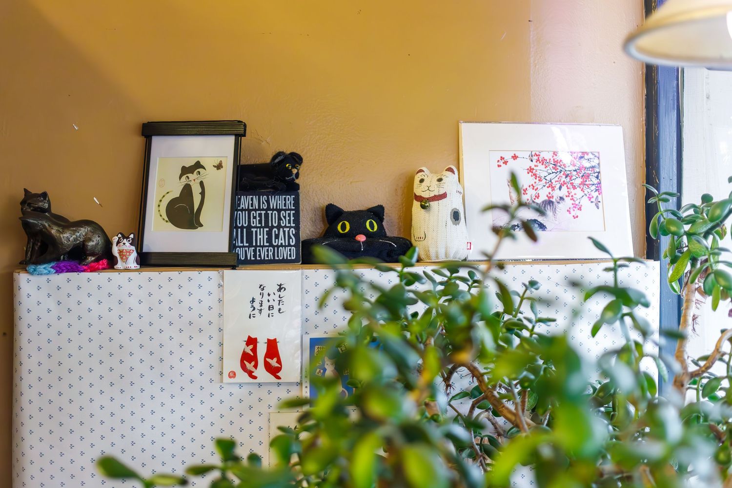 Decorative shelf display with cat figurines and artwork among potted plants.