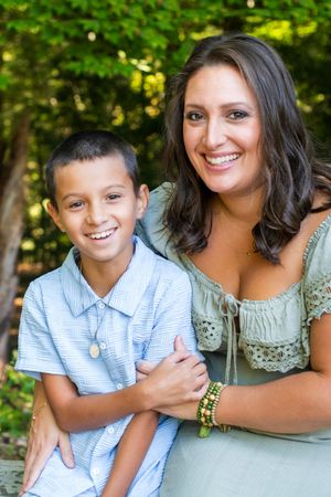 Smiling mother and young son posing together outdoors in a lush green park setting.