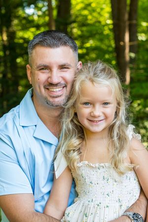 Happy father hugging his blonde daughter outdoors in a green forest background.