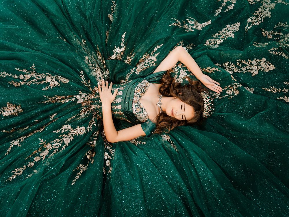 A person in an emerald green gown lies on the floor surrounded by shimmering sequins in a glamorous fashion pose.