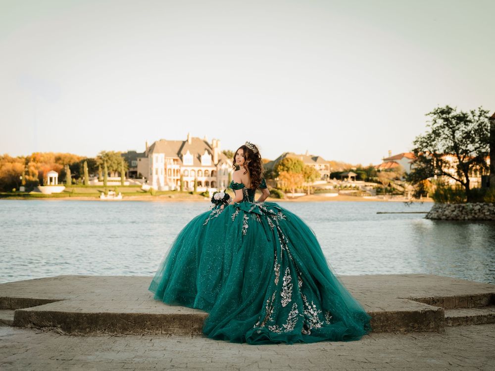 A teal ballgown dress flows elegantly along a lakeside path during golden hour.