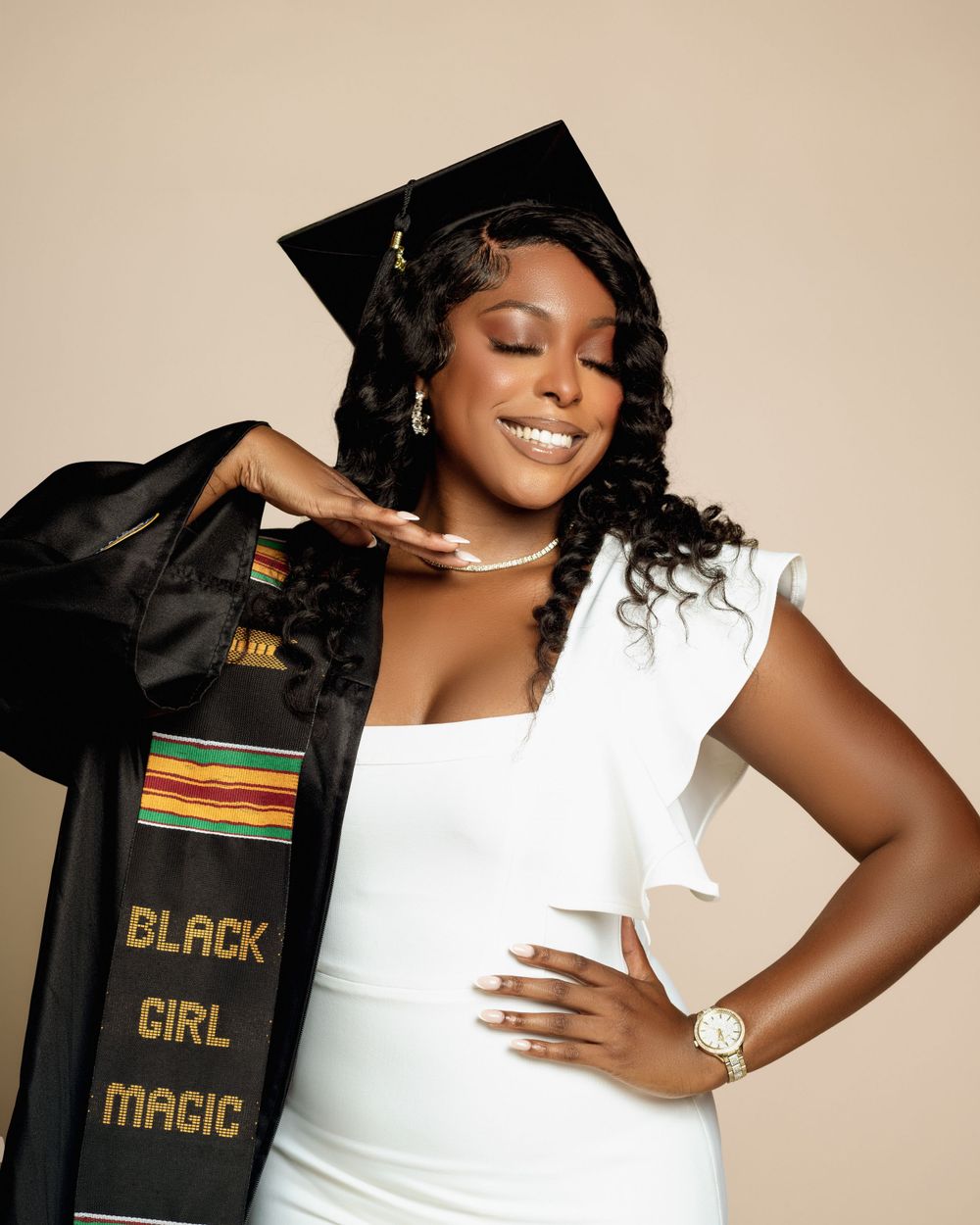 Graduate in white dress and black cap with decorative stole reading 'Black Girl Magic'.