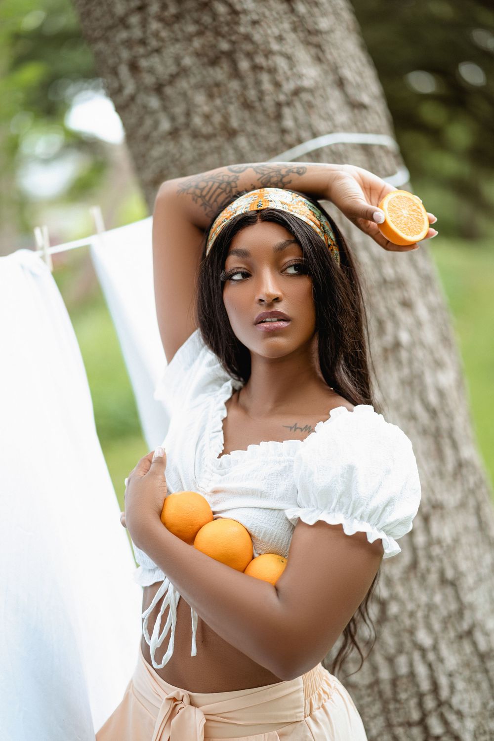 Woman in white crop top holds oranges in outdoor cottage core themed photoshoot.