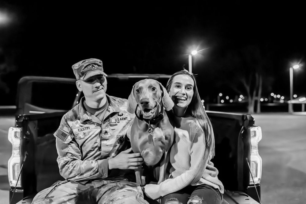 Military family sits in pickup truck bed with happy dog.