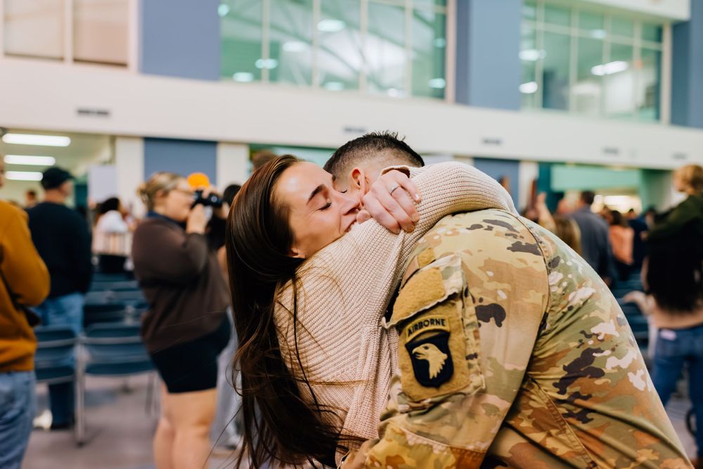 Emotional military reunion moment captured in busy indoor space.