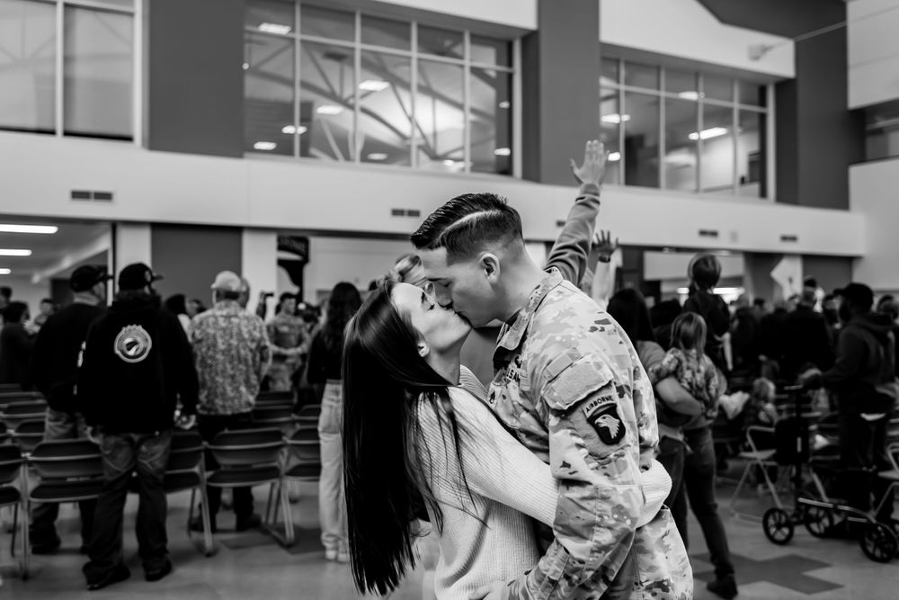 Black and white photo of military homecoming in crowded indoor facility.