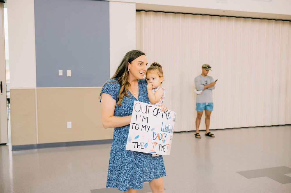 Mother and child hold welcome home sign in indoor venue.