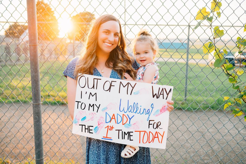 Family standing by fence at sunset holding sign for military homecoming.