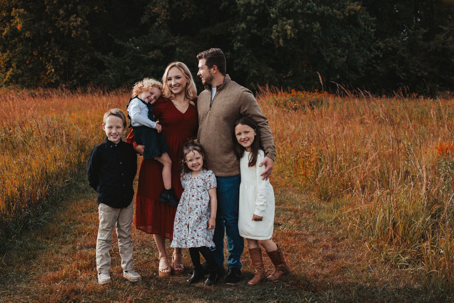 Family gathering in autumn field with warm sunset lighting and rustic outdoor setting.