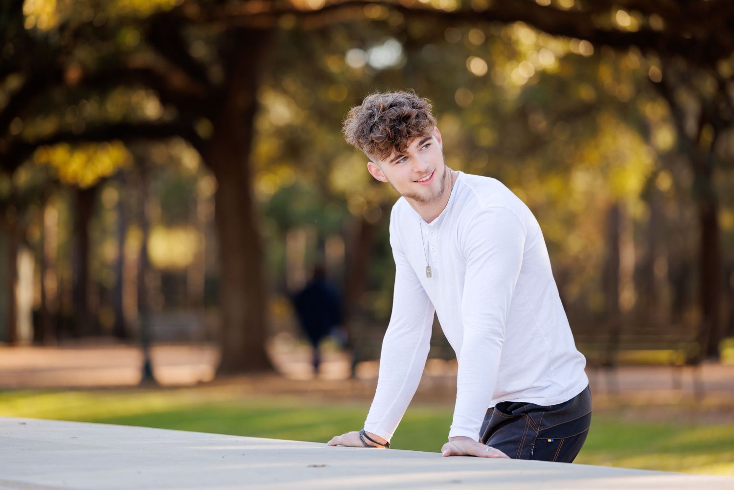 A casual portrait of a young person leaning on a wall in an autumn setting.