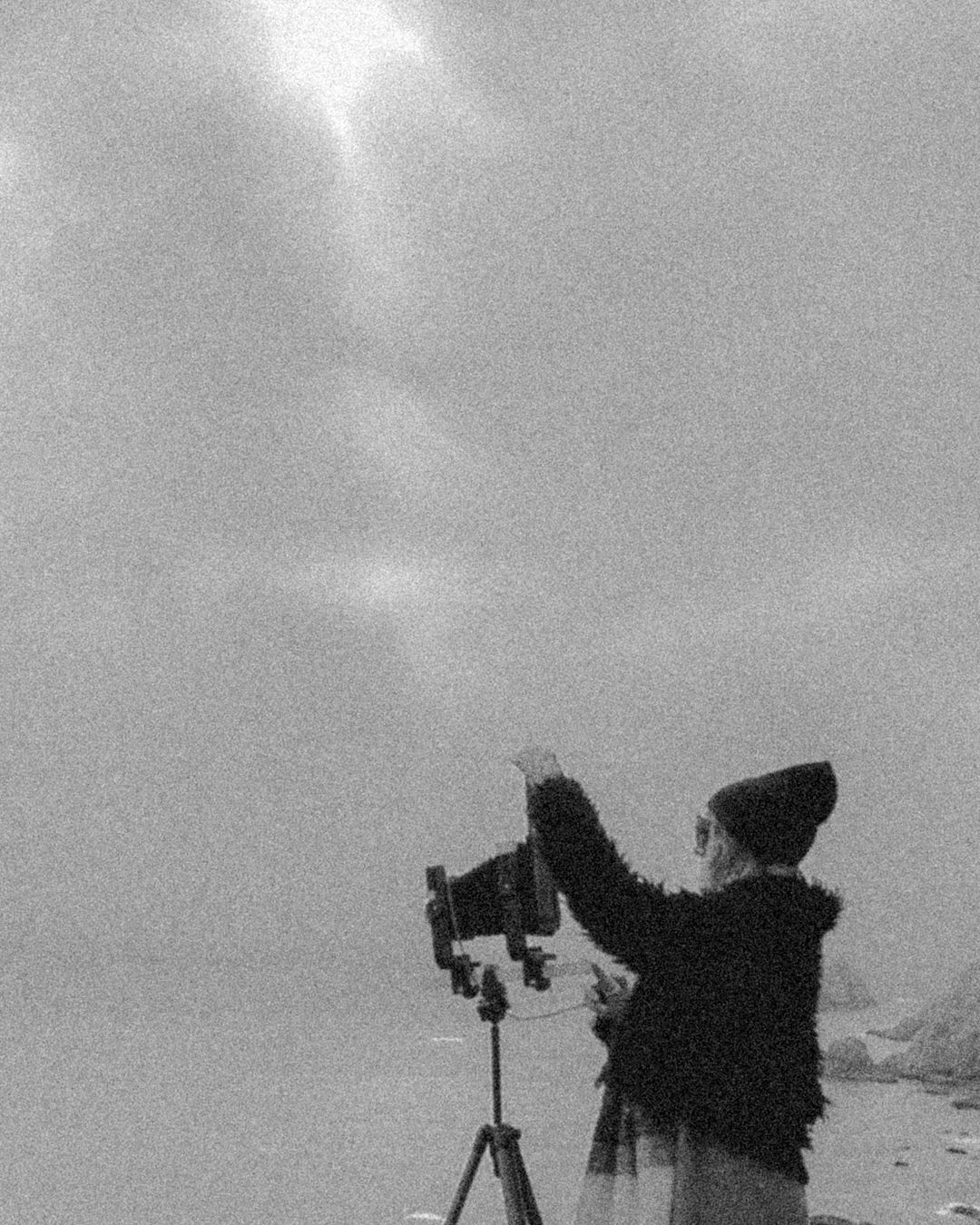 Silhouette of a photographer with a tripod camera against a misty sky.