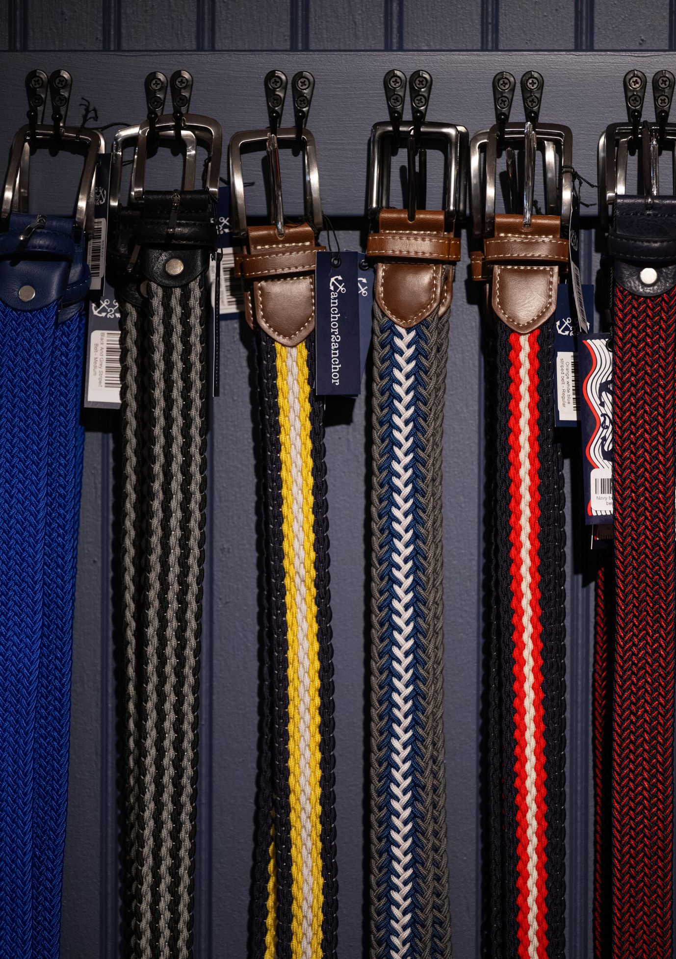 Collection of colorful leather belts hanging on retail display rack against dark background.