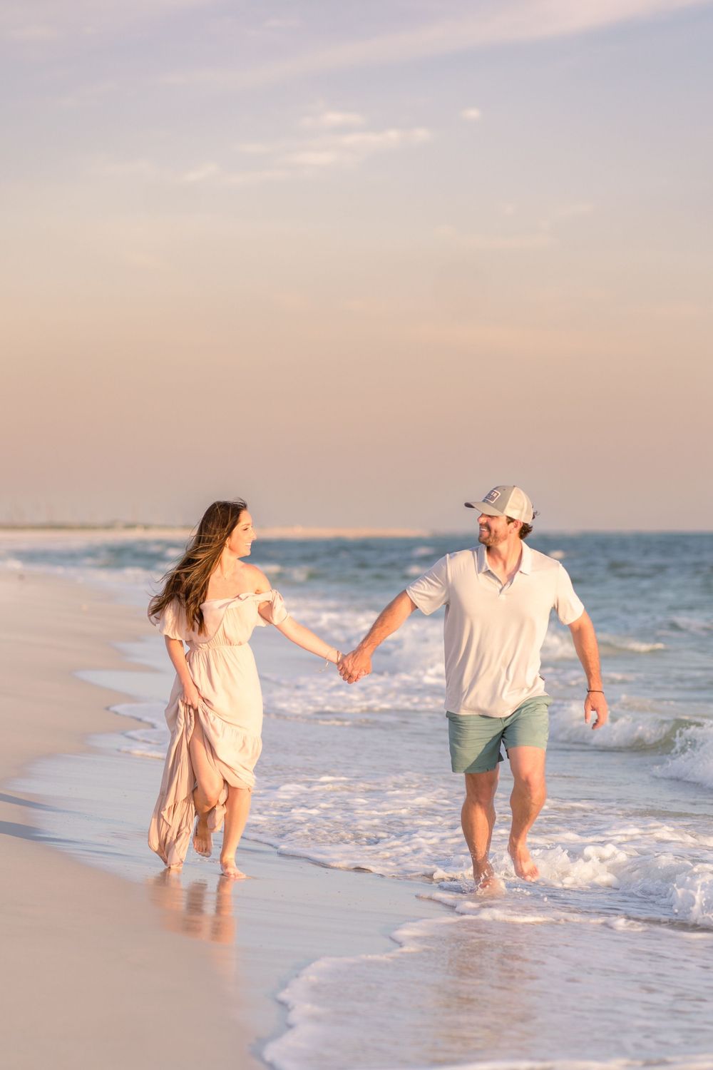 Happy couple holding hands and running through ocean waves on a sandy beach at sunset.