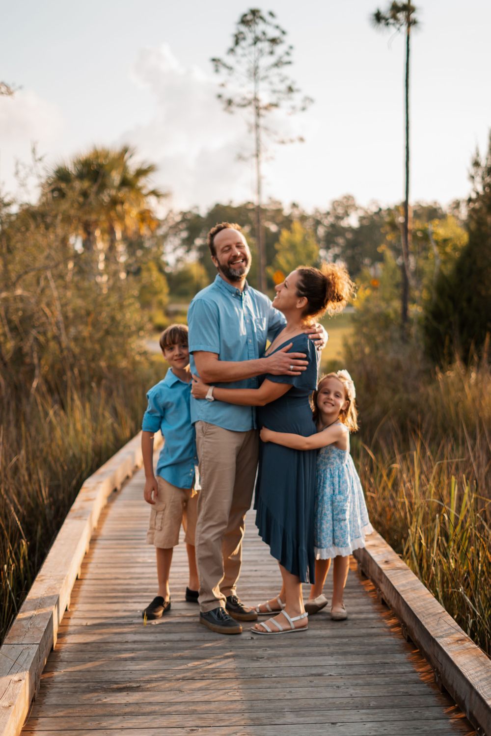 Happy family of four embracing on wooden boardwalk surrounded by Florida wetland nature.