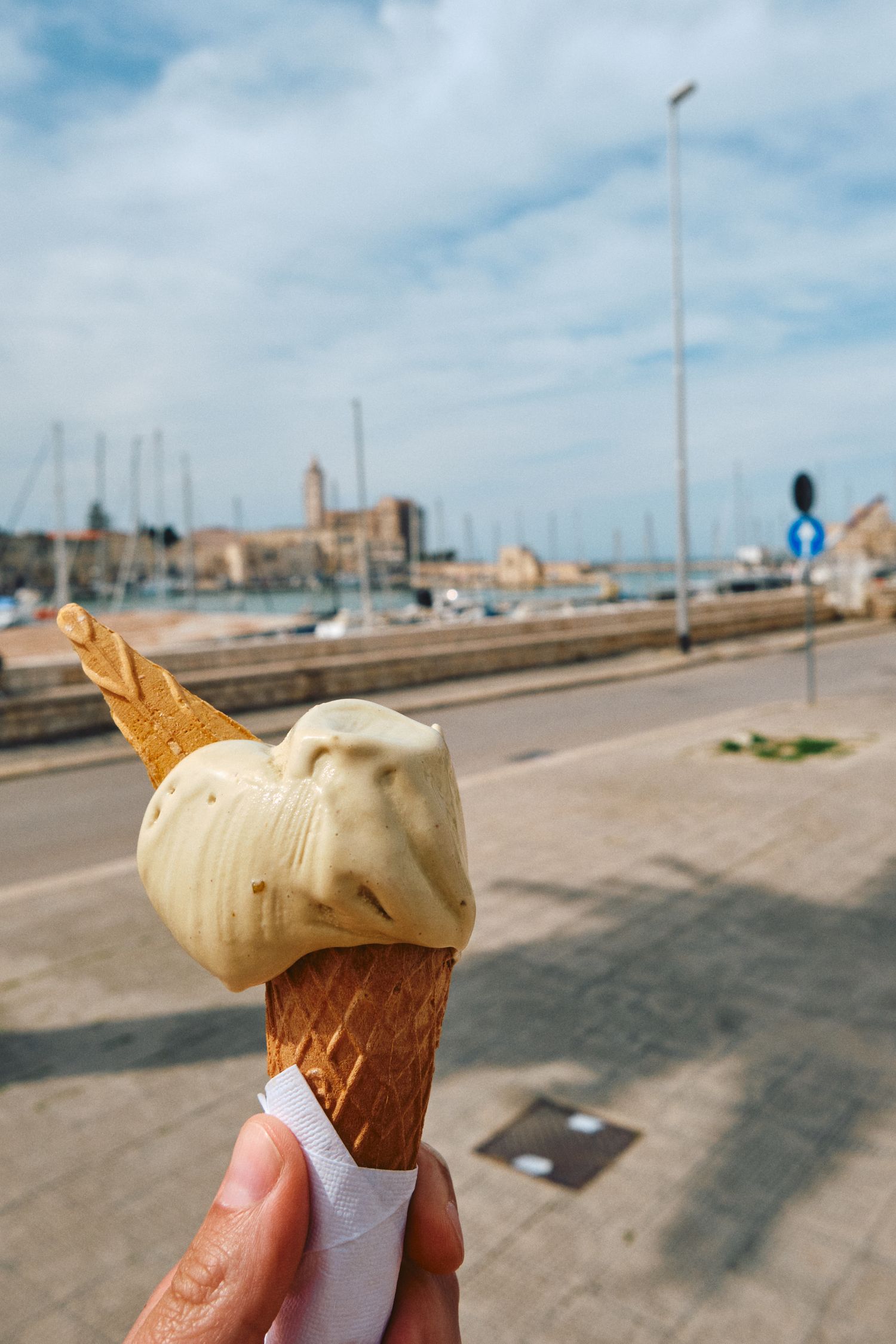 A vanilla ice cream cone held up against a coastal harbor background.