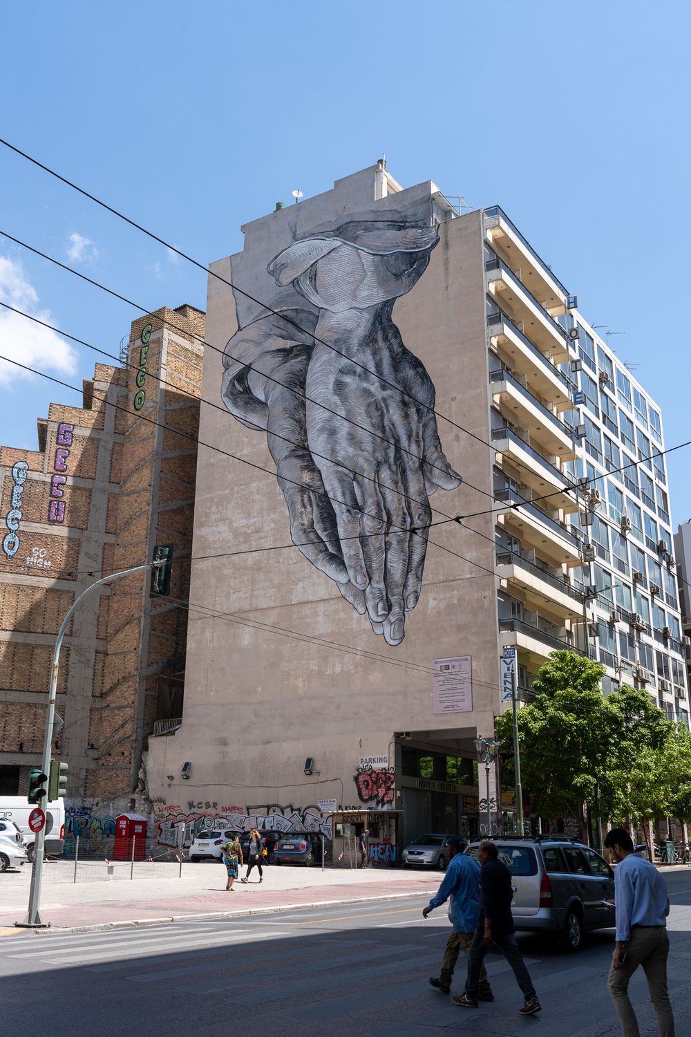Large-scale monochromatic street art mural depicting hands on urban building facade.