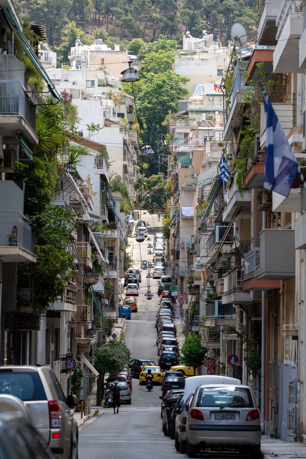 Steep urban street lined with apartment buildings and parked cars in Athens.