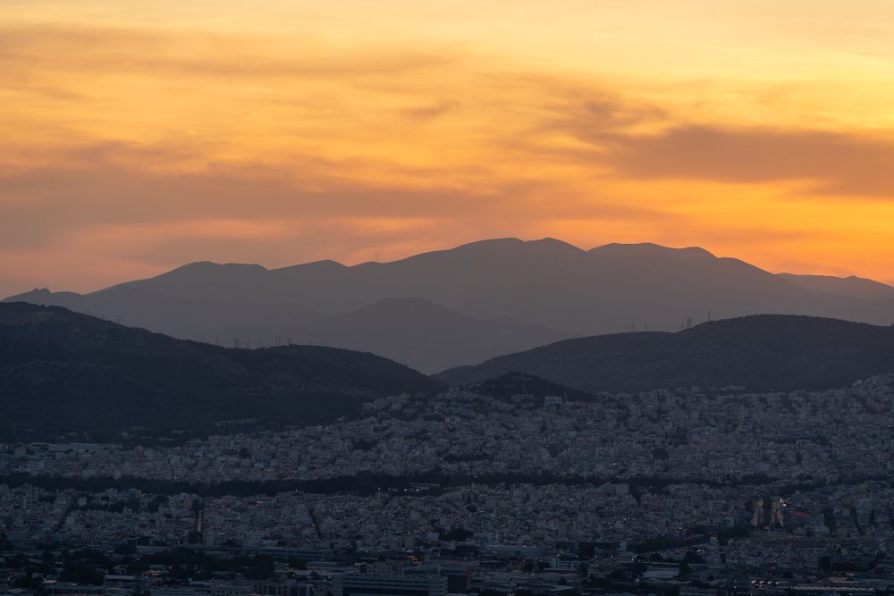 Dramatic sunset silhouettes mountains against an orange sky over Athens.