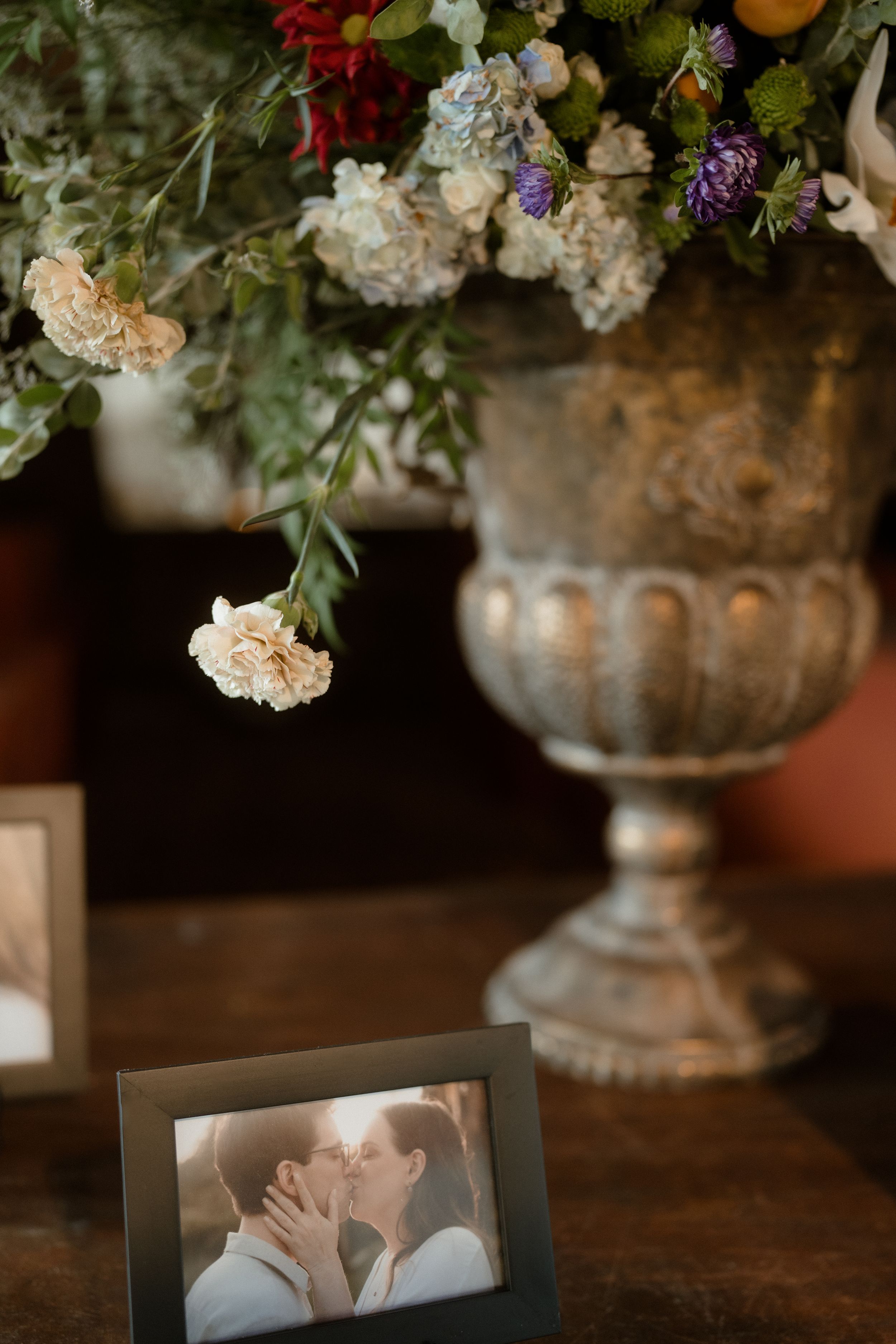 Elegant floral arrangements and photographs displayed on a dark wooden table at a wedding reception.