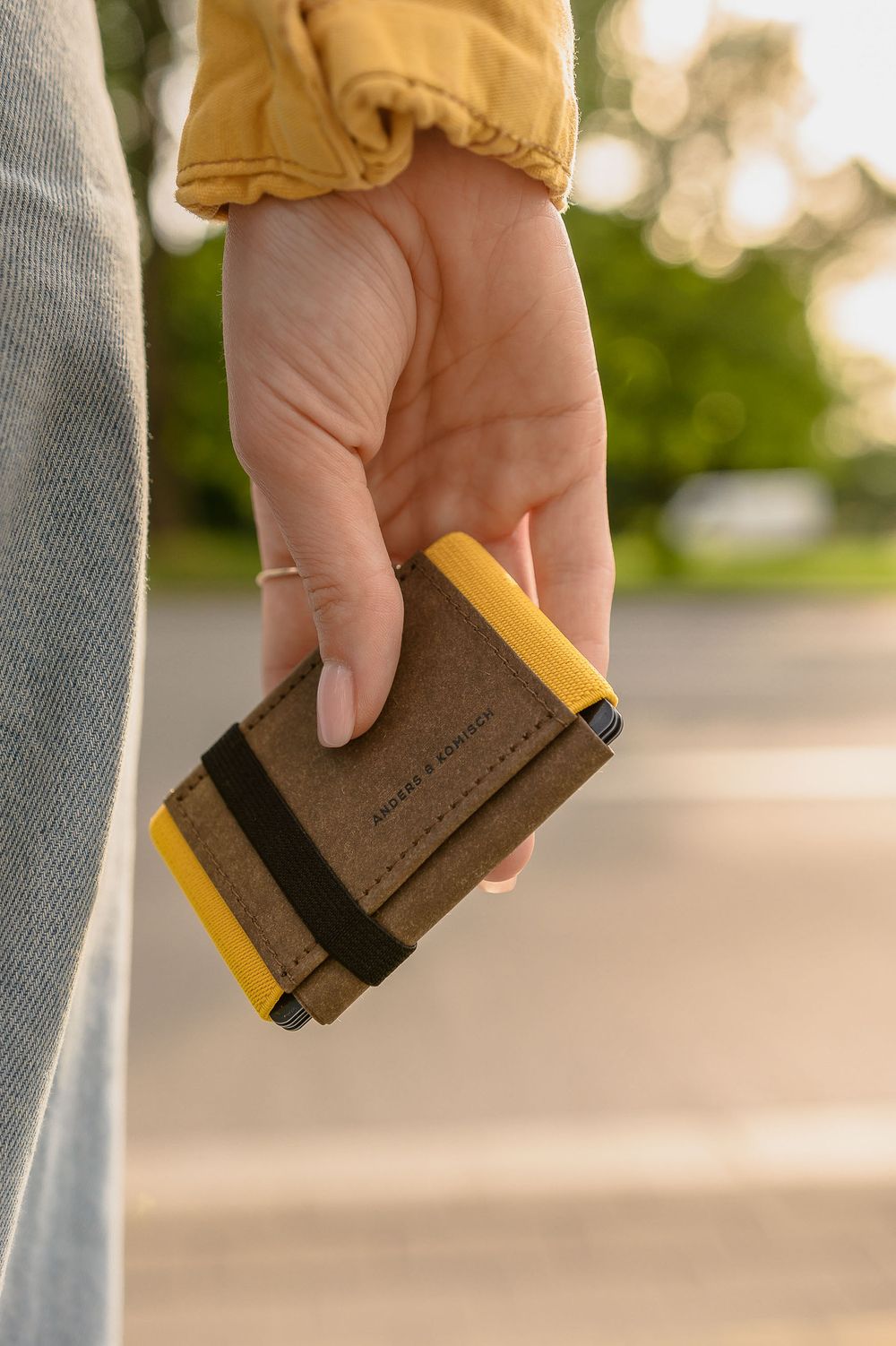 Close-up of hand holding compact brown leather wallet outdoors.