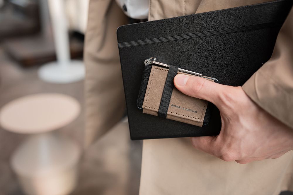 Hands holding a black and brown leather wallet with minimalist design details.