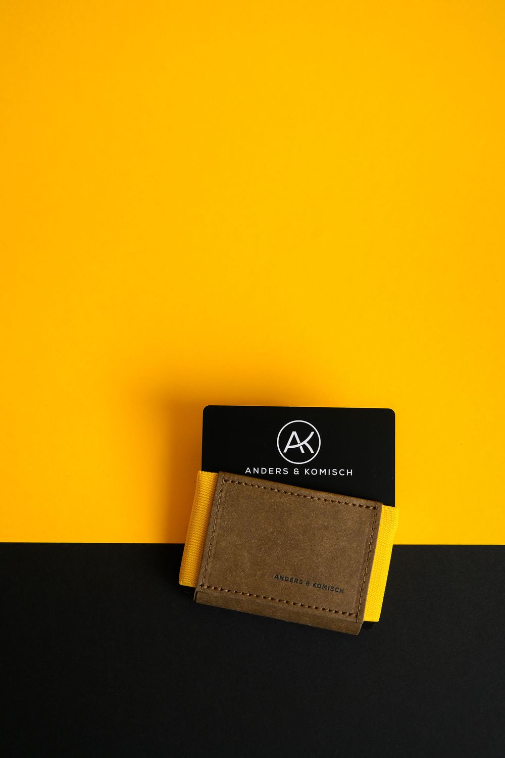 Stylish brown leather wallet with black label against vibrant yellow and black backdrop.