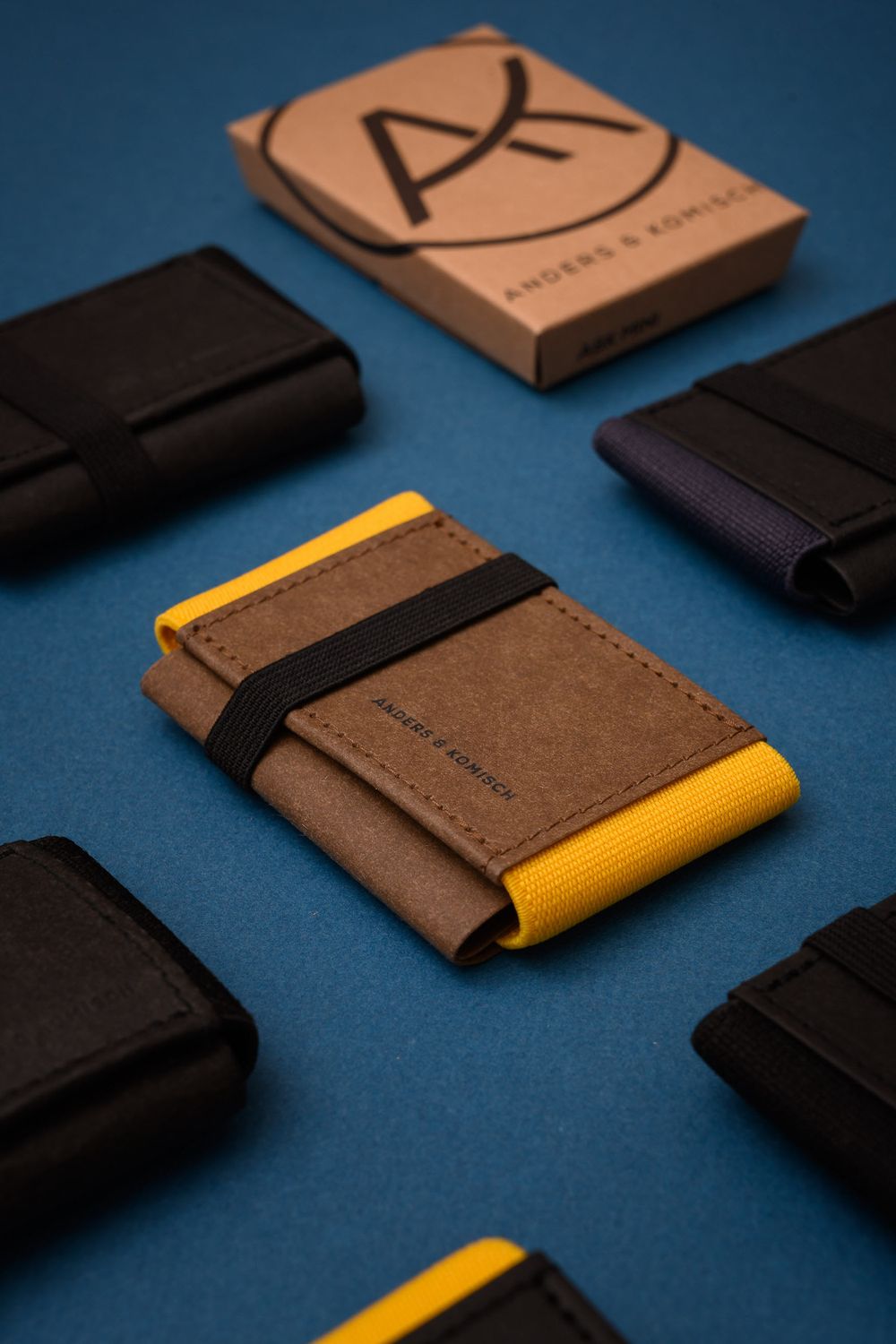Stylish leather wallets in brown and black with yellow accents displayed on blue background with minimalist packaging box.