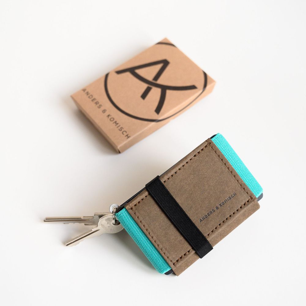 Minimalist handcrafted wallet in taupe leather with turquoise accents and silver keys shown with branded packaging.