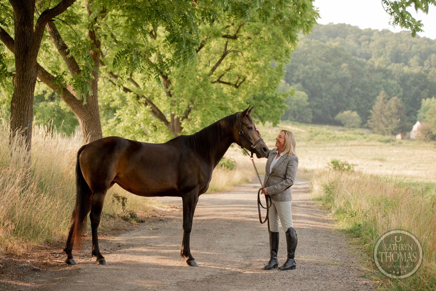 Dark horse and handler share a moment on a tranquil tree-lined path.