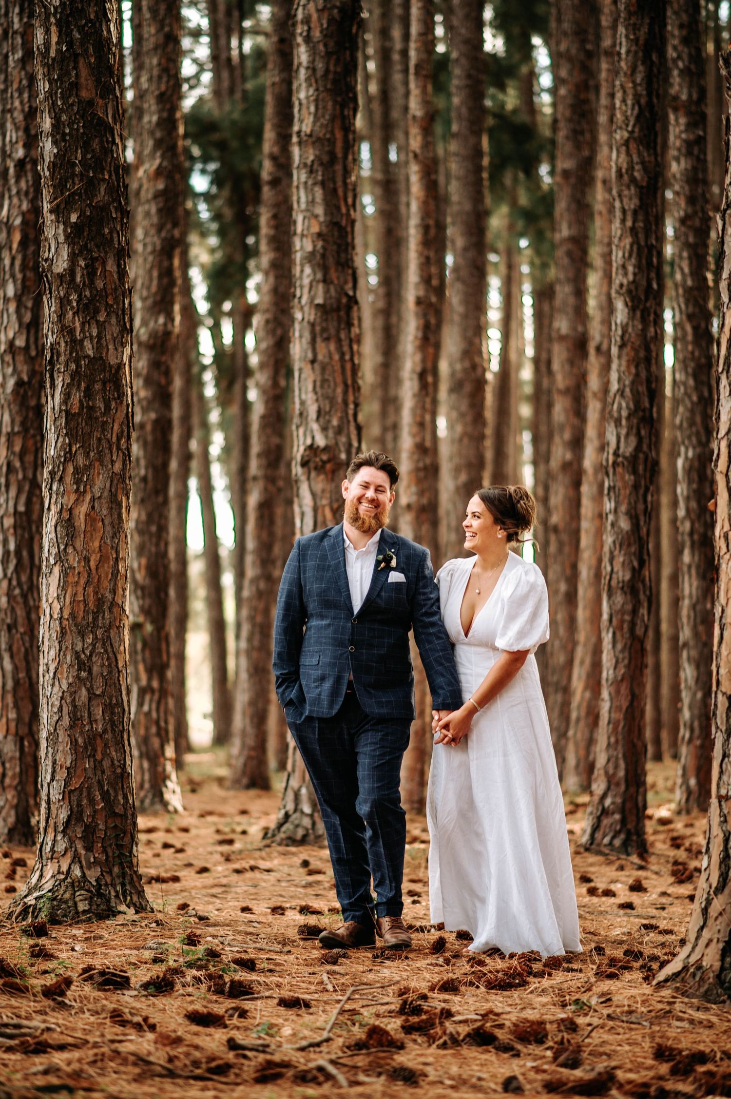 A wedding couple standing together in a forest of tall pine trees.