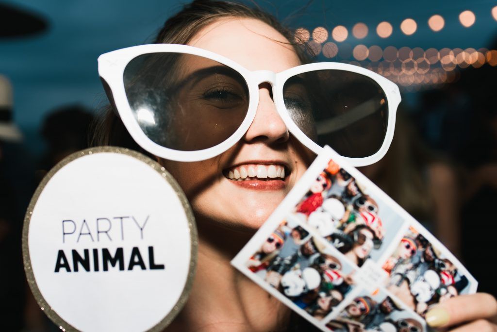 A laughing woman holds oversized white sunglasses and a Party Animal sign at a celebration.