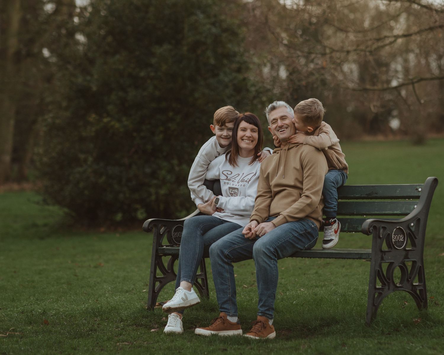 Family relaxing together on wooden park bench surrounded by autumn trees.