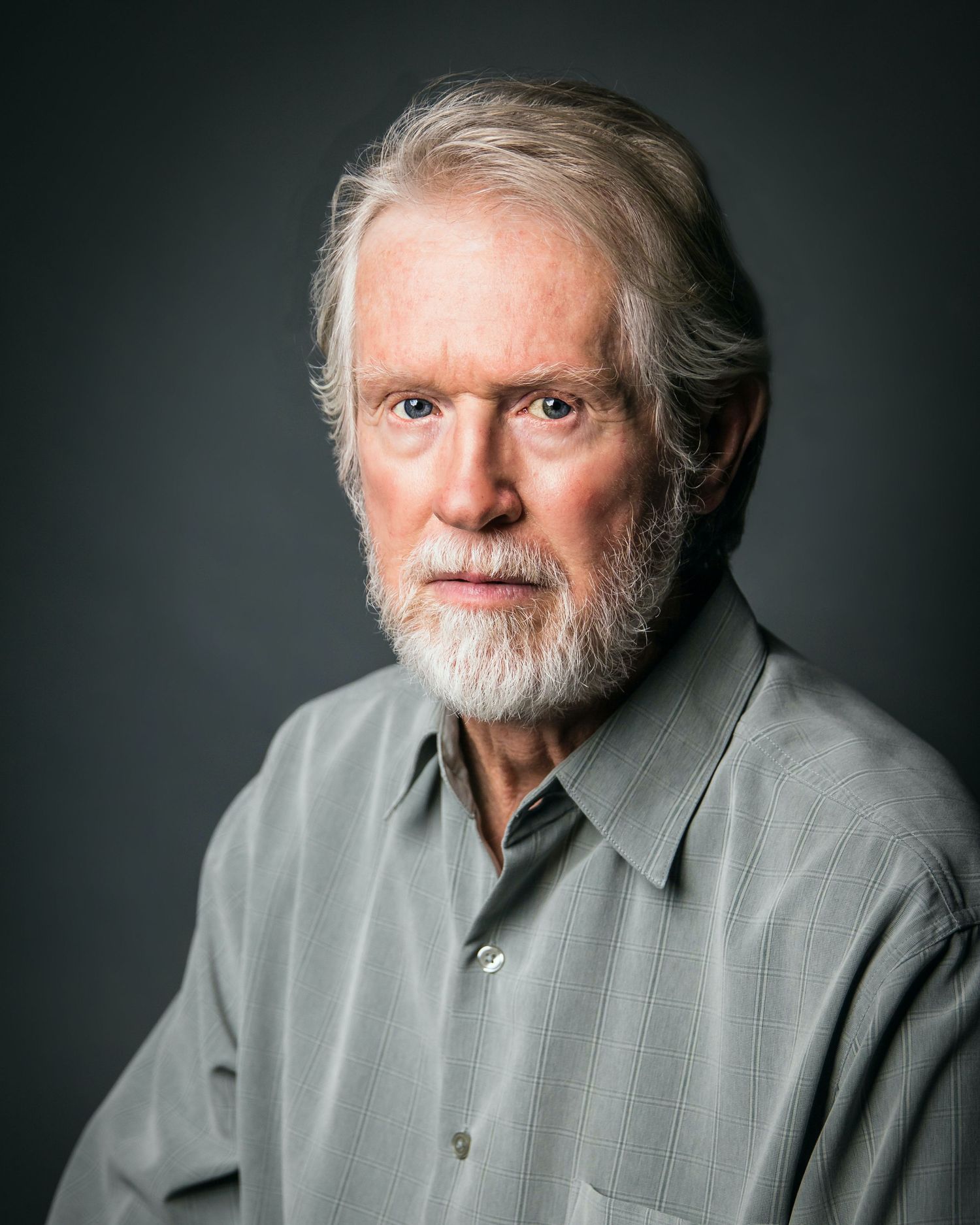 Professional studio portrait of an older gentleman with gray hair and beard wearing a casual button-up shirt.