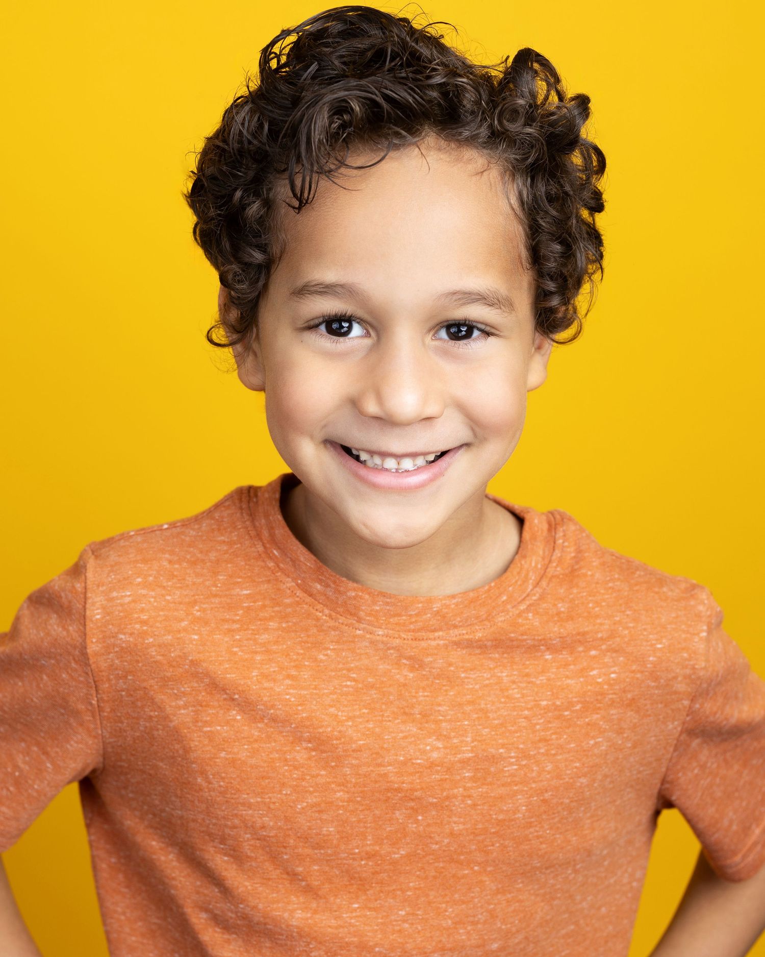 Child wearing an orange sweater making different playful expressions against a bright yellow background.