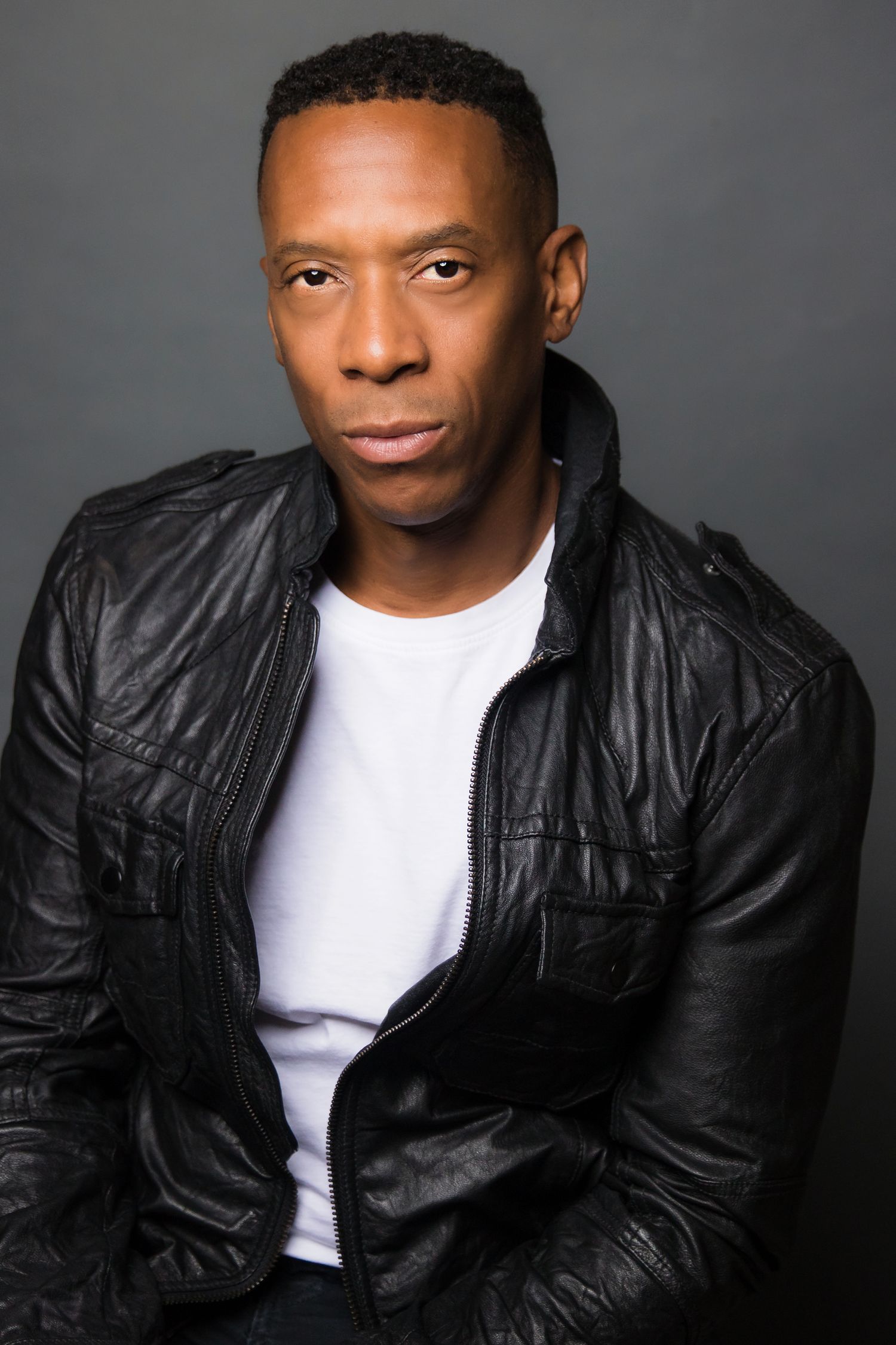 Dramatic portrait of a person wearing a black leather jacket against a dark background.