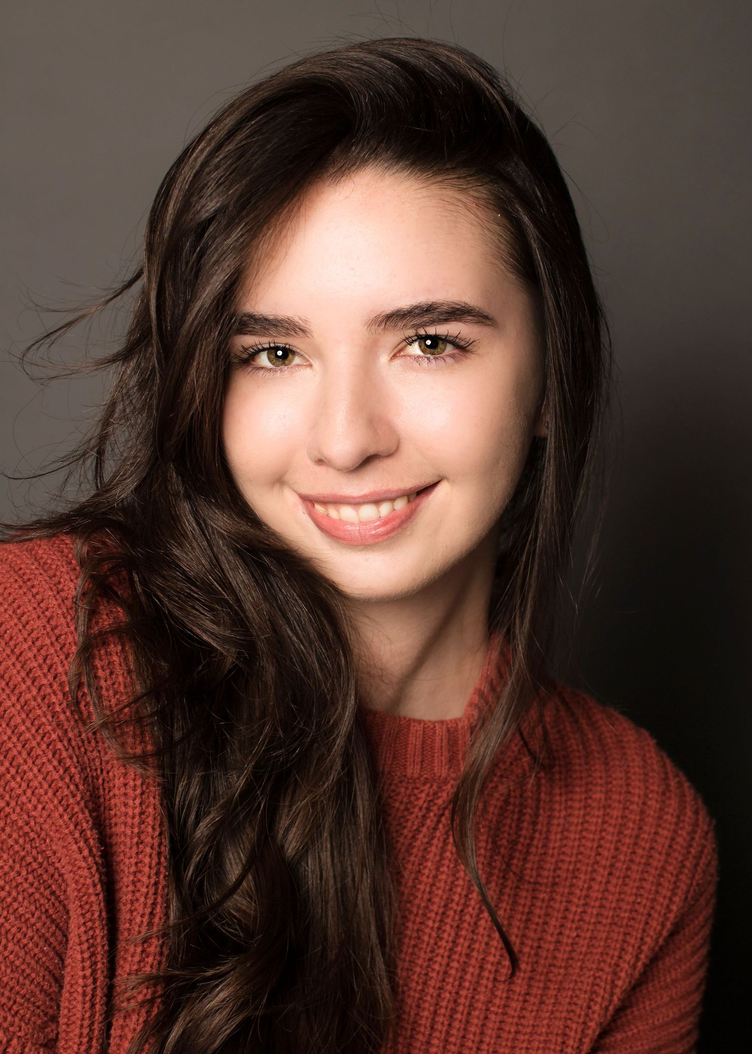 Professional headshot of a person in a burgundy sweater with long dark hair and natural makeup.