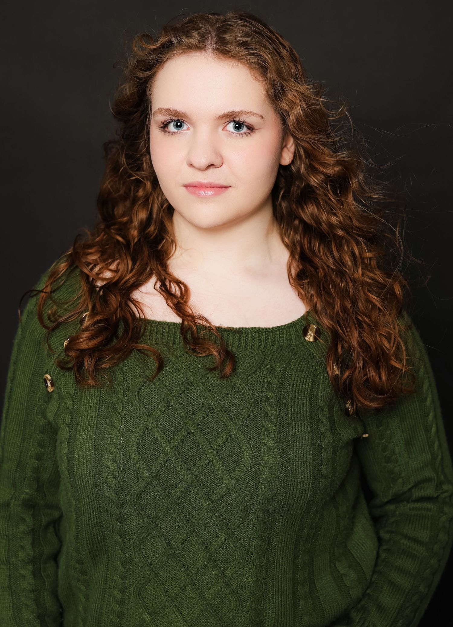 Portrait wearing a green cable knit sweater against dark background.