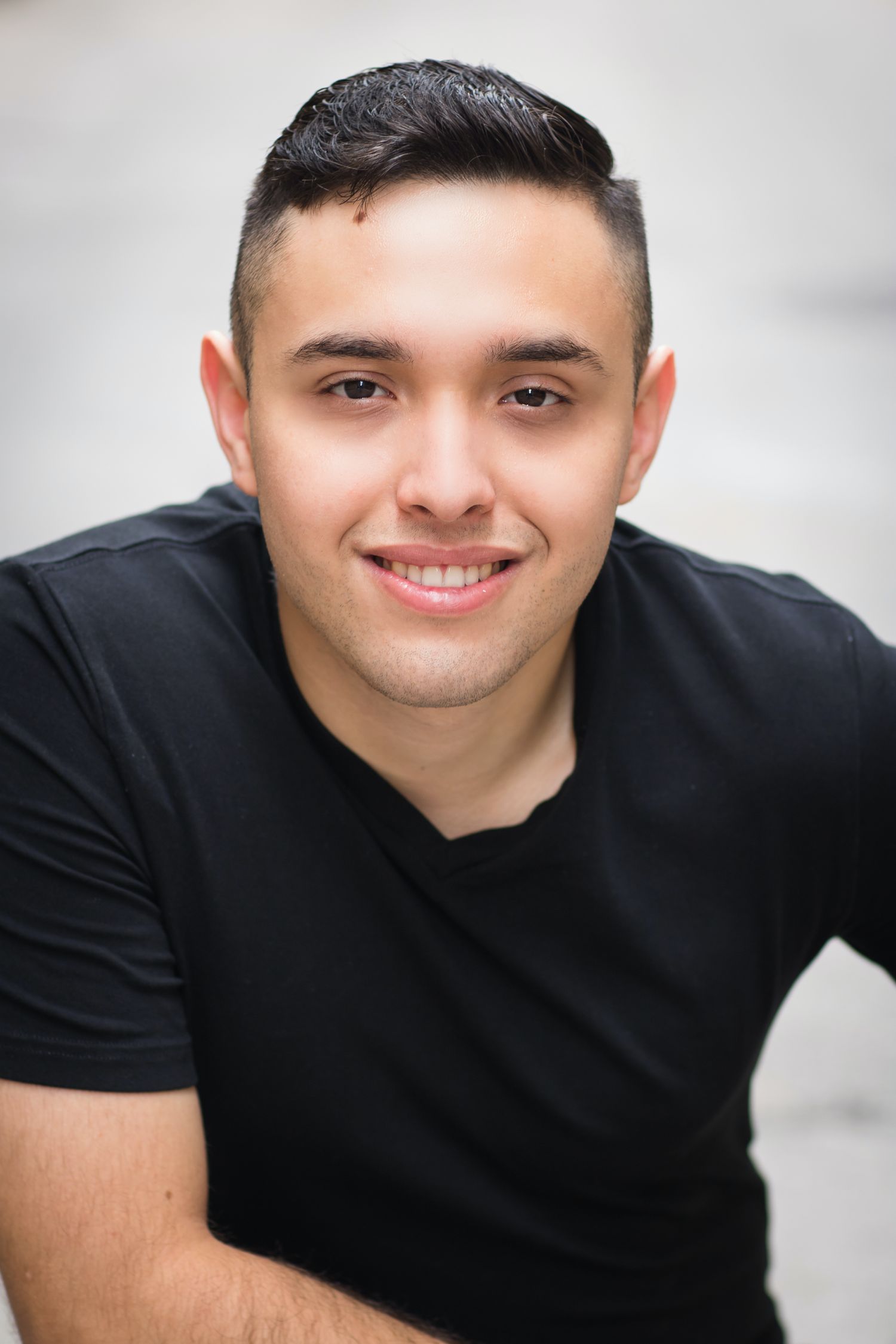 Professional headshot of a person in a black t-shirt with a warm smile against a light background.