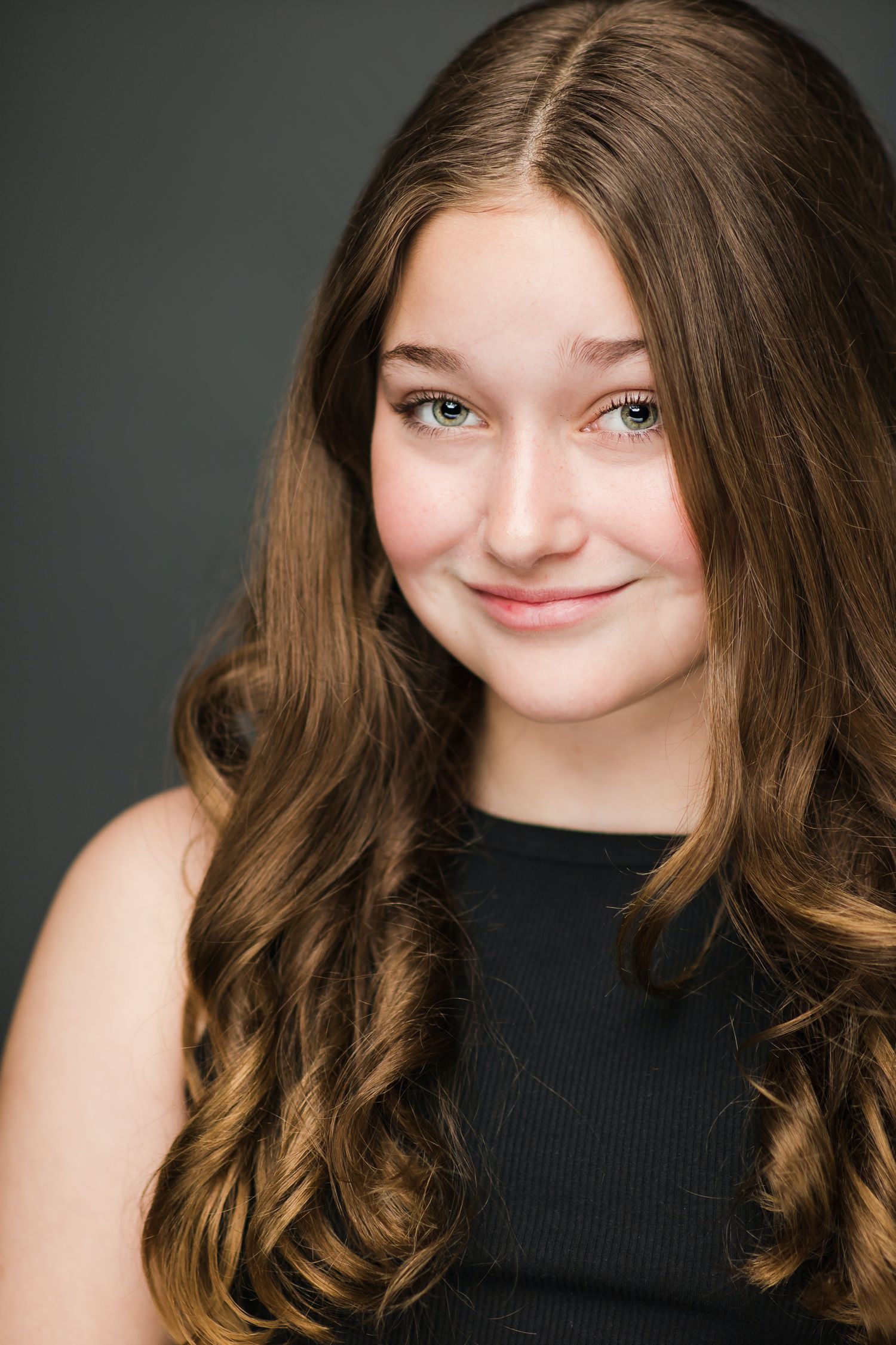 Professional headshot of a young woman in black top with long wavy brown hair.